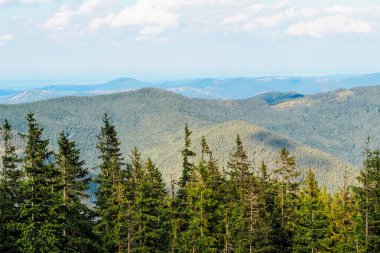 Yeşilliklerle kaplı uçsuz bucaksız dağlar, berrak mavi gökyüzünün altında doğal güzellik ve sükuneti sergiliyor..