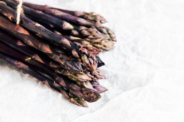 Bir demet taze mor kuşkonmaz sicimle birbirine bağlanır ve hafif desenli bir yüzeye yerleştirilir..