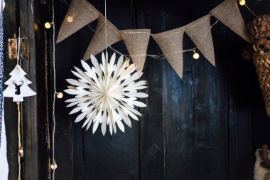 Dekoratif beyaz bir kağıt yıldız, koyu ahşap bir zemin üzerinde bir çuval bezi pankartıyla asılı. Kutlamalar için mükemmel sıcak bir ortam yaratıyor..
