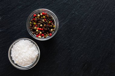 Koyu taş bir yüzey üzerinde cam kaselerde çeşitli biberler ve kaba tuz pişirmeye hazırdır..