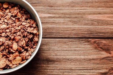 Bir kase tahıl gevreği, sade bir kahvaltı için mükemmel bir ahşap masaya davetkar bir şekilde oturur. Doğal dokular sıcak bir atmosfer yaratır..