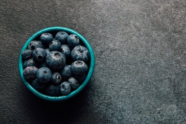 Taze yaban mersiniyle dolu canlı bir turkuaz kâse sağlıklı yemek veya tatlı malzemesi için mükemmel desenli koyu bir yüzeye oturur..