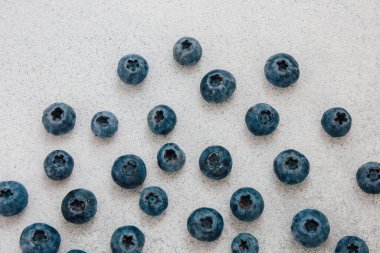 Yuvarlak dolgun yaban mersinleri açık gri bir yüzeye yayılmış canlı renklerini ve taze kalitelerini sergiliyorlar..