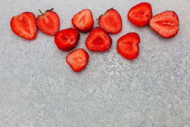 Parlak kırmızı çilekler ikiye ayrılır ve sanatsal olarak gri bir zemine dağılır. Canlı renklerini ve tazeliklerini sergilerler..