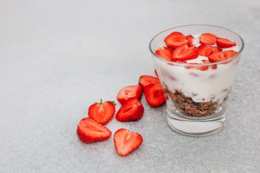 Yoğurt parfe, açık gri bir yüzeye yerleştirilmiş kremalı yoğurtlu gevrek ve canlı taze çilek katmanları içerir..