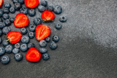 Dilimlenmiş çilek ve yaban mersininden oluşan canlı bir gösteri onların tazeliğini ön plana çıkaran koyu bir arka planda belirir..