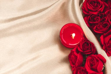 Sıcak bir atmosfer, kırmızı güller ve pürüzsüz bir bej kumaşa yerleştirilmiş bir mum ile oluşturulur. Samimi anlar için mükemmel..
