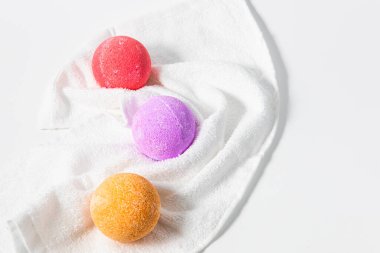 Kırmızı mor ve turuncu renkte üç banyo bombası beyaz bir havluda zarif bir şekilde otururlar. Rahatlamak için canlı renklerini ve dokularını sergilerler..