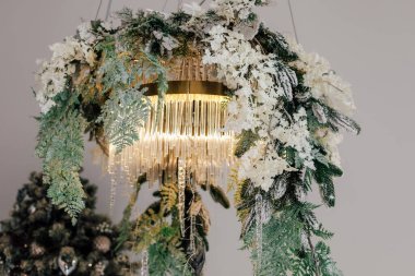 Yeşillik ve narin beyaz çiçeklerle bezenmiş eşsiz bir avize samimi bir odayı aydınlatıyor ve şenlikli bir atmosfer yaratıyor..