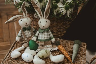 Şenlikli tavşanlar, bahar dekorasyonu için dokuma sepetine dizilmiş renkli Paskalya yumurtası ve havuçlarının arasında otururlar..
