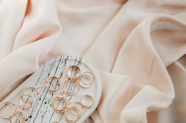 Yüzükler ve küpeler basit bir tabakta güzelce düzenlenmiş yumuşak akışkan kumaş üzerinde zarafet ve cazibe yayıyor..