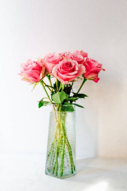 Pembe bir gül buketi parlak renkleri ve zarafetiyle alanı aydınlatan şeffaf cam bir vazoda zarif bir şekilde duruyor..