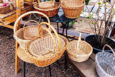 Güneşli bir bahar gününde, çeşitli boylarda renkli dokuma sepetler, bir açık hava pazarında ahşap masaların üzerinde sanatsal eserler sergiliyor..