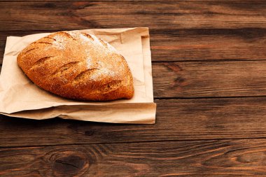 Bir somun kabuklu ekmek kahverengi kağıdın üzerinde duruyor altın kabuğunu ve dokusunu kırsal bir ahşap masaya vurguluyor..