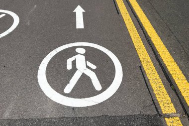 Net bir yaya sembolü, bir şehir caddesinde yaya geçidini gösteriyor. İnsanları sarı çizgilere karşı güvenli bir şekilde yürüme yönüne götürüyor..