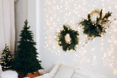 Parıldayan ışıklarla dolu güzel dekore edilmiş bir oturma odası Noel ağaçları ve duvarda zarif çelenkler sıcak bir şenlik havası yaratıyor..