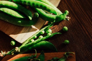 Sağlıklı yeşil bezelyeler ve kabuklar ahşap bir yüzeyde sanatsal olarak dizilmiş. Sıcak doğal ışık onların canlı renklerini vurguluyor..