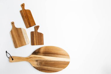 Farklı şekillerde ve boyutlarda tahta kesme tahtaları temiz beyaz bir yüzeye dizilir ve doğal tasarım ve dokularını gösterir..