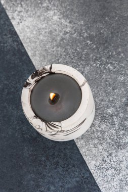 Hafif yanığı olan dekoratif bir mum farklı renklerde desenli bir yüzeye oturur. Alev nazikçe titreyerek sıcak bir ortam yaratır..