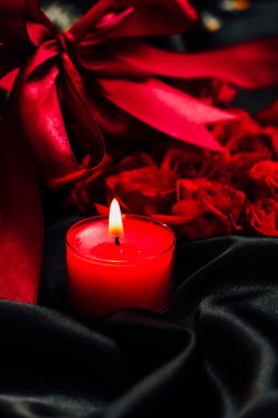 Kırmızı bir mum hafifçe titreşir yemyeşil güller arasında ve saten bir kurdele romantizm için mükemmel bir ortam yaratır..