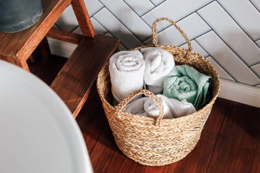 Dokuma sepetinin içinde, dinlendirici bir banyoda havlular var. Tahta bir tabure uzaya kırsal bir dokunuş ekler..