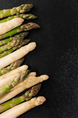 Türlü taze yeşil ve beyaz kuşkonmaz sapları özgün renklerini ve dokularını gösteren koyu bir yüzeyde güzelce düzenlenmiştir..