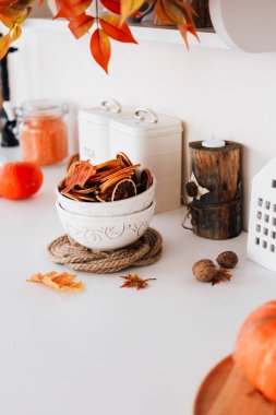 Bir kase kurutulmuş meyve mutfak tezgahında dekoratif yapraklar ve kırsal unsurların yanında duruyor ve davetkar bir sonbahar atmosferi yaratıyor..