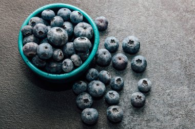 Taze yaban mersiniyle dolu bir turkuaz kasesi dokulu bir yüzeyde duruyor ve yakınlarda böğürtlenler var..
