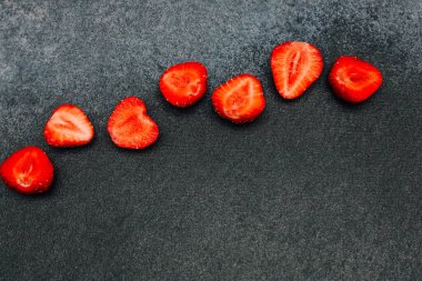 İkiye bölünmüş taze kırmızı çilekler, canlı renklerini ve sulu dokularını gösteren koyu desenli bir yüzey üzerinde düzgünce düzenlenmiştir..