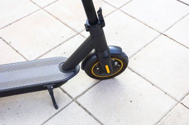 Şık, siyah bir elektrikli scooter gün ışığında şehir ortamında asfalt bir yüzey üzerinde durur ve sürücüyü bekler..