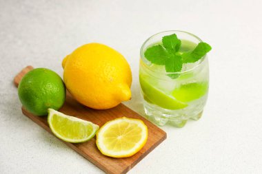 Limon ve limondan yapılmış canlı bir içecek tahta bir tahtanın üzerinde taze meyvenin yanında oturur. Sahne parlak ve davetkar bir atmosferi yansıtıyor..