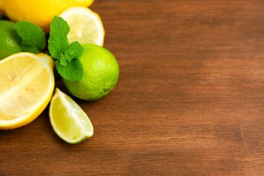 Parlak limonlar ve limonlar ahşap bir yüzeyde sanatsal olarak düzenlenir. Nane yaprakları mutfak yaratımı için mükemmeldir..