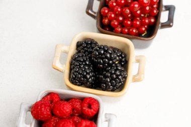 Üç küçük konteynır, böğürtlen, ahududu ve kırmızı frenk üzümleri de dahil olmak üzere çeşitli taze böğürtlenler sergiliyor..