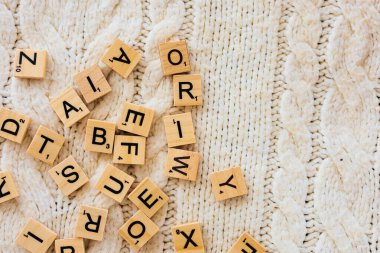 Yumuşak örgü bir battaniyeye serilmiş ahşap bir Scrabble koleksiyonu evde eğlenceli bir kelime oyunu oynamaya davet ediyor sıcak öğleden sonraları için mükemmel..