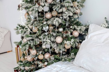 Parlak süsler ve dekorasyonlarla süslenmiş bir Noel ağacı rahat bir yatağın yanında duruyor ve rahat bir atmosfer yaratıyor..