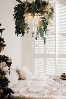 Konforlu bir yatak odasında çarpıcı bir bitki düzenlemesi yumuşak yatak örtüsü ve sıcak bir atmosfer oluşturan tatil dekorasyonu bulunur..