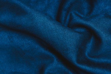 Koyu mavi kumaş düz bir yüzey üzerinde pürüzsüz ve buruşuk yatar. Yumuşak dokusunu ve parıltısını nazikçe iç mekan aydınlatmasında gösterir..