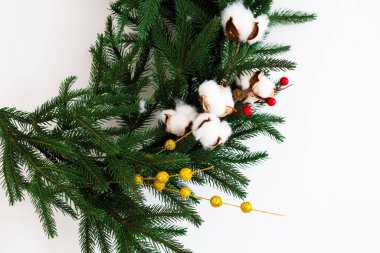 Pamuk tokaları, kırmızı böğürtlenler ve altın aksanlarla süslenmiş her daim yeşil dallardan yapılmış güzel bir Noel çelengi. Tatil dekorasyonu için mükemmel. Şenlikli bir ortam yaratmak için ideal..