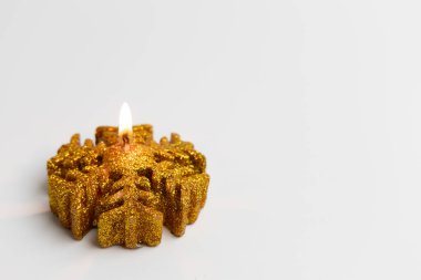 Kar tanesi şeklindeki parıltılı altın bir mum, yumuşak, sıcak bir parıltı saçıyor. Parlak süslemeler temiz beyaz bir yüzeye yerleştiriliyor ve kutlamalar için mükemmel bir şenlik atmosferi yaratıyor..