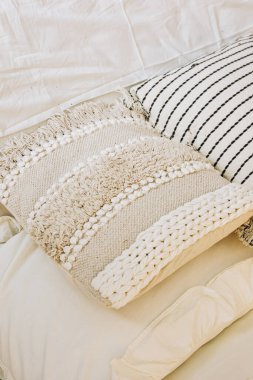 Yumuşak ve desenli dekoratif yastıklar nötr renkli bir yatak örtüsü üzerinde şekillendirilir ve sabah ışığında rahat bir atmosfer yaratır..