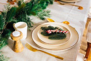 Noel düzenlenmiş yemek masasında zarif tabaklar ve çatal bıçak bulunur. Taze yeşillik ve şeker kamışı bayram için sıcak bir atmosfer yaratacak şenlikli bir dokunuş ekler..