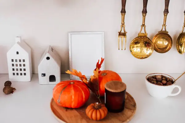 Turuncu balkabakları bir mum ve küçük dekoratif bir balkabağının yanında ahşap bir tabakta otururlar. Altın mutfak aletleri, metin için boş çerçeve alanı olan rahat mutfak ortamının kırsal duygusunu geliştirmek için yukarıda asılı.