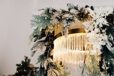 Güzel bir avize, buzlu yeşillik ve sıcak bir atmosfer yaratan narin ışıklarla süslenir. Sahne, şık bir iç mekanda kış dekorunun özünü yakalıyor..