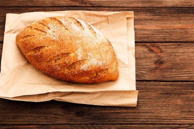 Esnaf ekmeğinin altın sarısı bir somunu tahtadan bir masanın üzerinde kahverengi bir kağıt parçasına oturur..