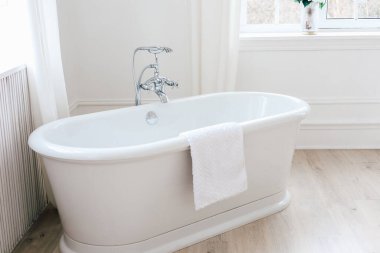 A spacious bathroom features a beautiful freestanding bathtub with a sleek design. Soft natural light streams through a window creating a calming atmosphere perfect for relaxation.