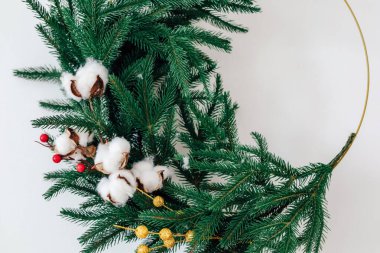 A beautifully crafted wreath featuring lush green pine branches white cotton bolls and red berries. This festive decoration is perfect for welcoming guests during the holiday season.