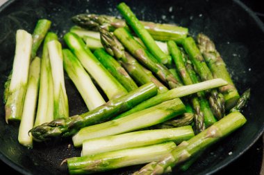 Bright green asparagus spears are sizzling in a skillet on the stovetop. The fresh vegetables are cut and arranged for cooking showcasing their vibrant color and healthy look in a home kitchen.