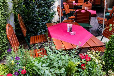 Taze çiçekler ile çevrili bir verandada ahşap masalarda renkli kırmızı masa örtüleri bulunan açık hava restoranında açık havada oturma