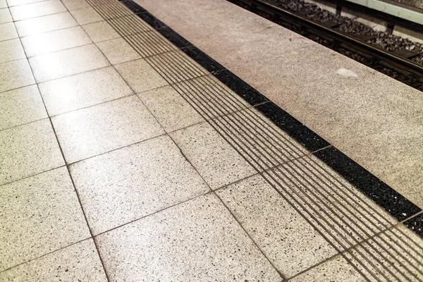 Image of speckled subway flooring with black trim and safety markings near train tracks