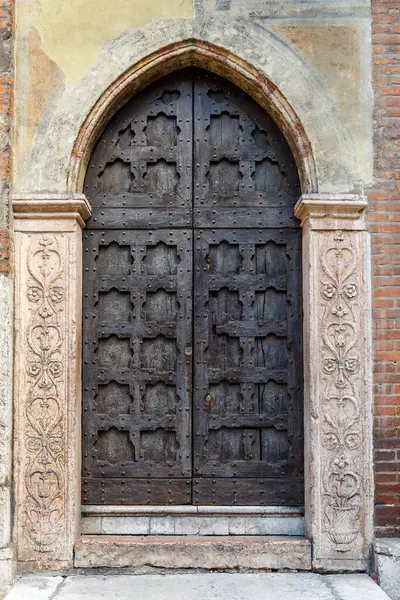 Ornate carved medieval door with metal studs in an arched stone surround with carved arabesque motifs in an exterior brick wall